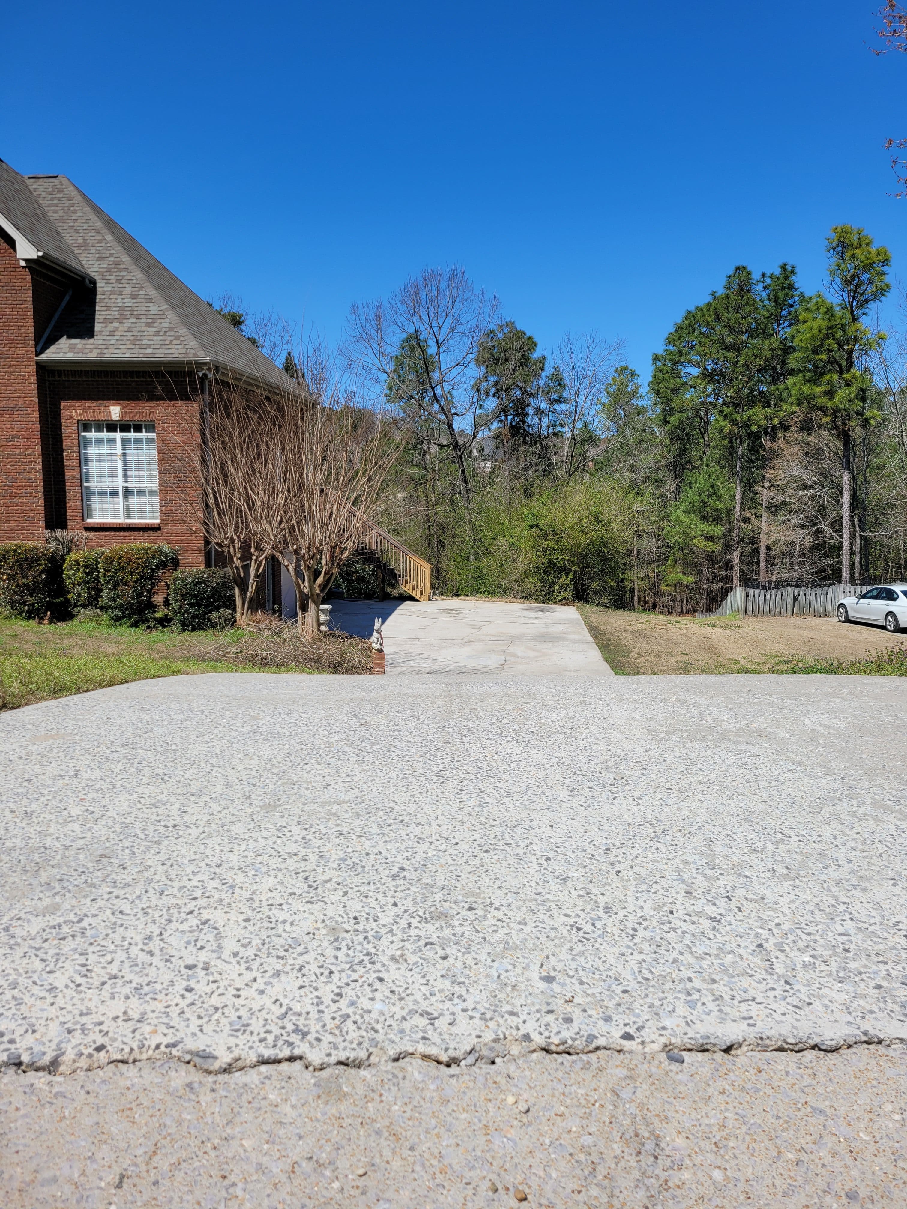 Residential driveway leading to a house with trees in the background and a clear blue sky.