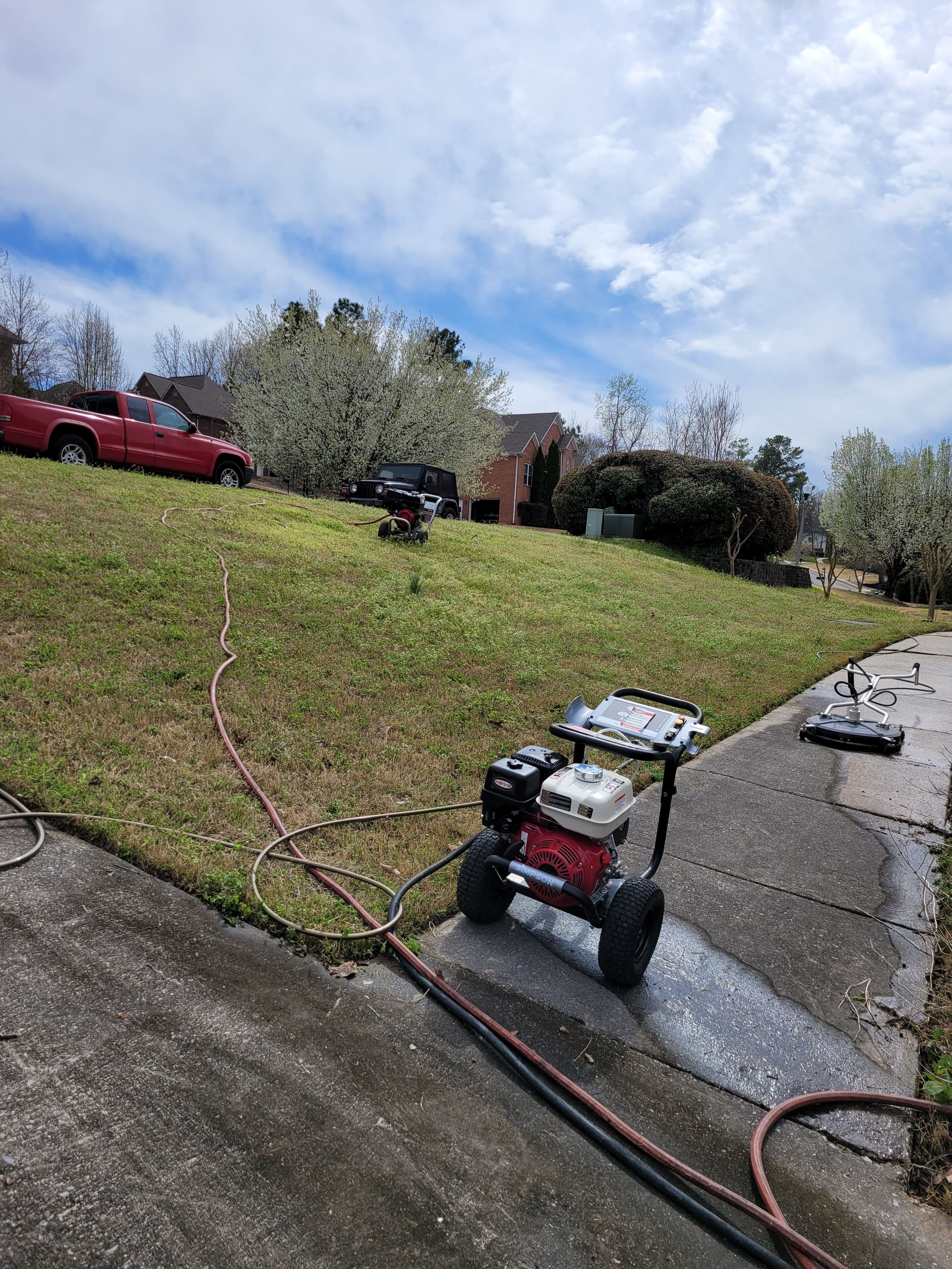 Pressure washer on driveway with grass and homes in the background, blue sky overhead.