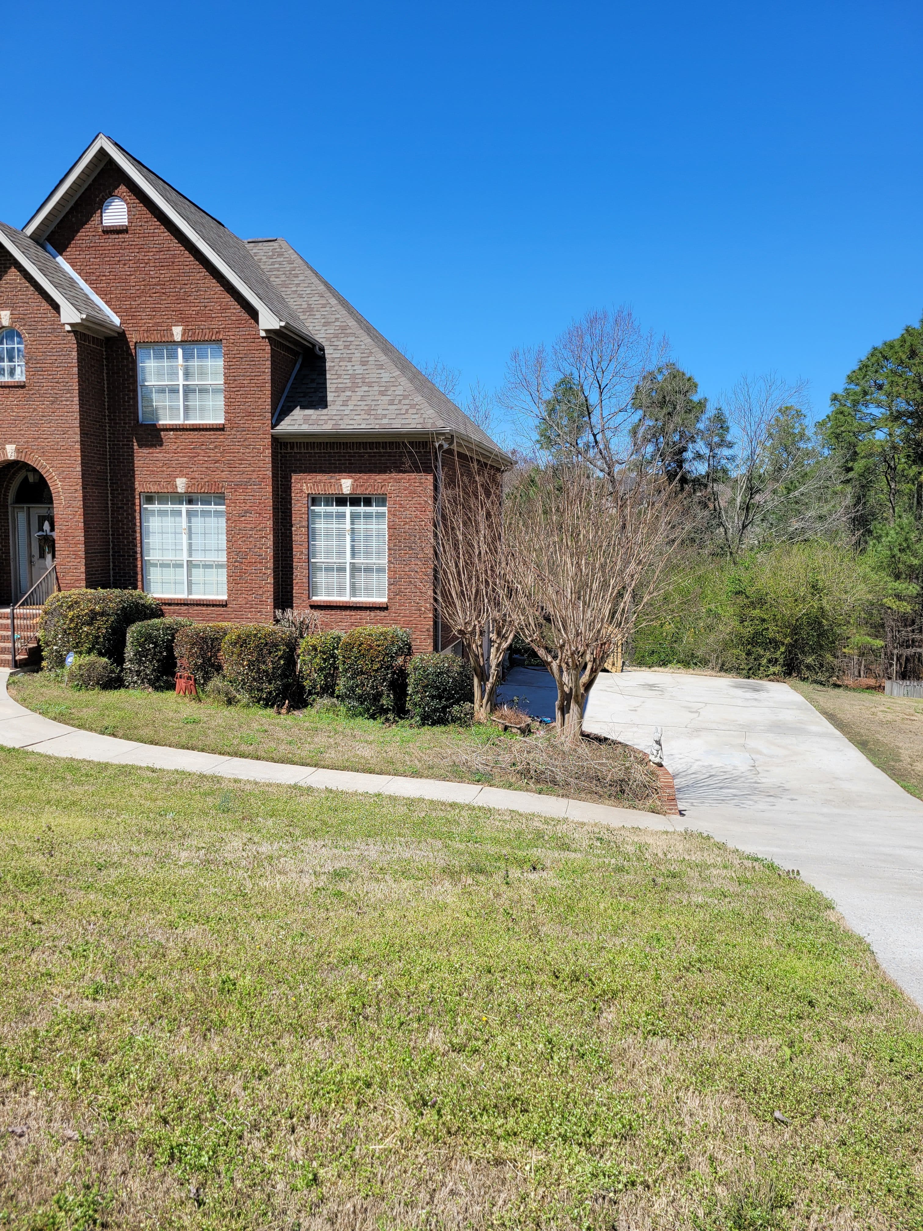 Brick house with landscaped yard and attached driveway under clear blue sky.